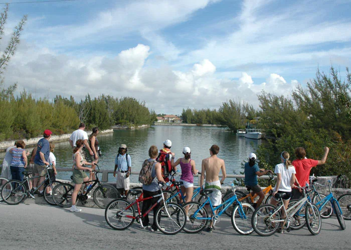 group of people stop riding their bicycles in front of a river as tour guide speaks in freeport
